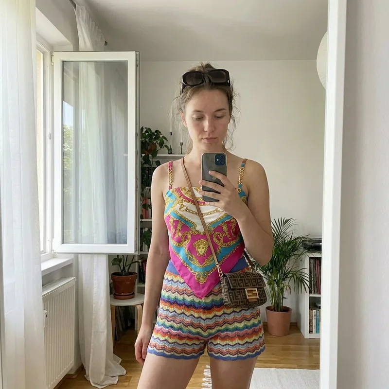 The same woman in the same pose wearing a colorful silk top and knit shorts after the AI clothes changer swapped her outfit